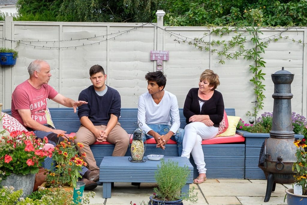 two adults and two students sitting on a bench in a beautifully landscaped garden talking together