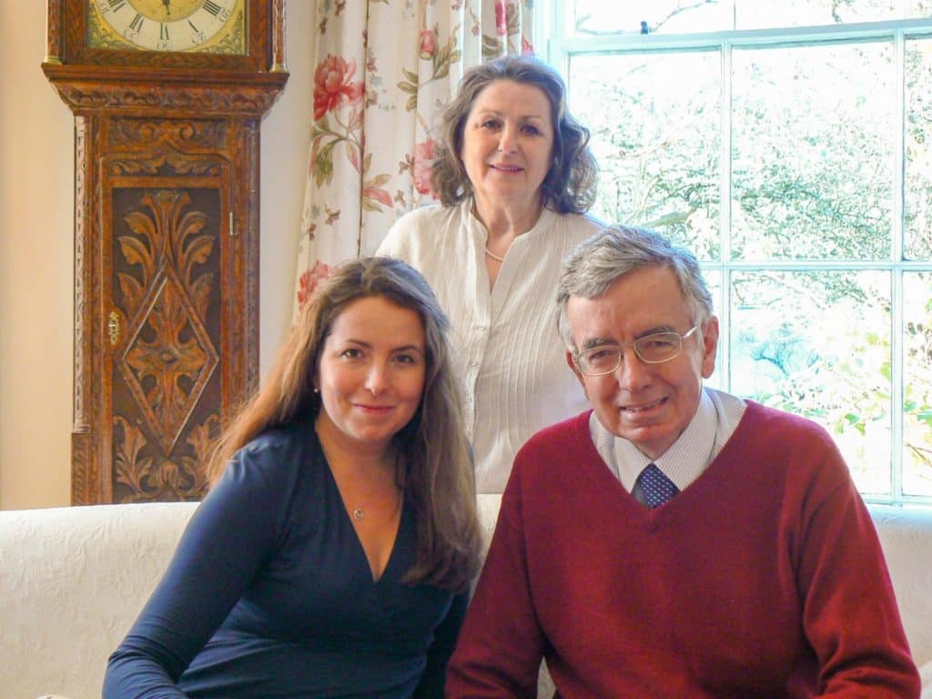 Richard and Jo Tomlinson with Sarah Tomlinson in their sitting room at the Isca School. There is a grandfather clock and an open window behind them
