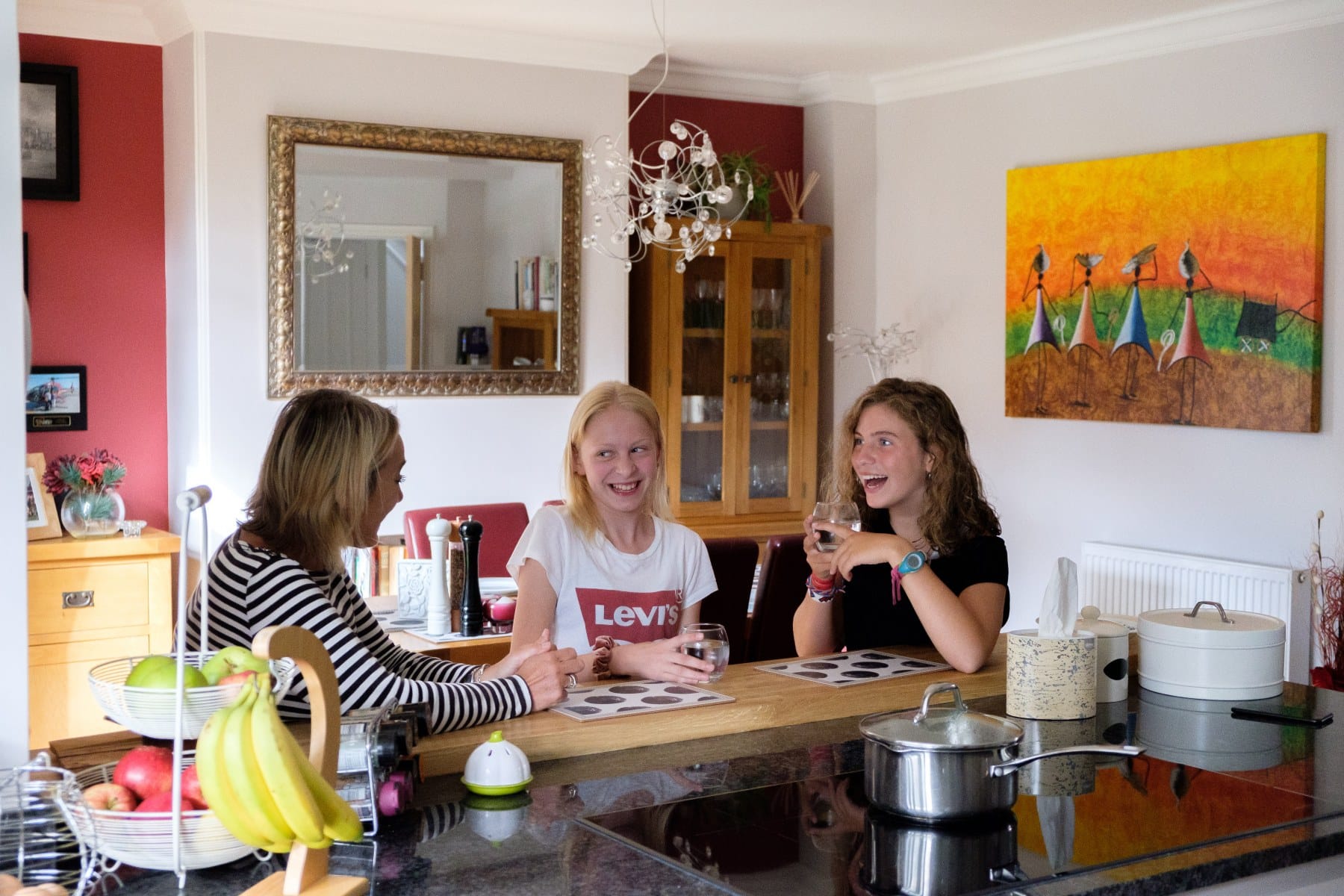 two young students chatting to their host mother and having a drink in a modern kitchen