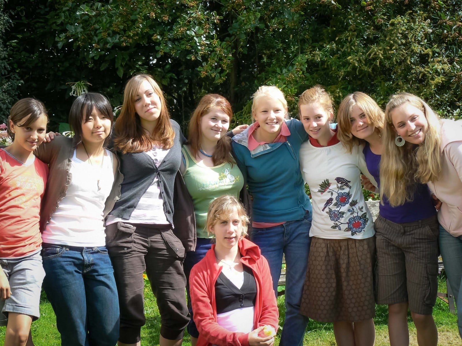 group of young girls with their arms interlocked smiling at the camera in the garden of the Isca School of English