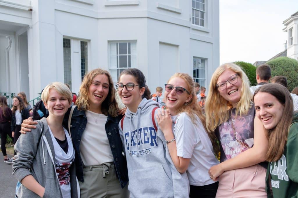 group of girls smiling and hugging in the front garden of the Isca School of English. One of them is wearing an Exeter Univeristy jumper